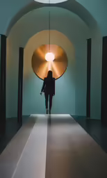 a person in black walking down the hall between a sculpture and light