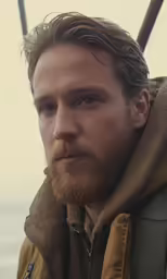 a man with a beard and brown hoodie stands next to a railing