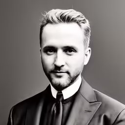 a male in a black suit and tie posing for the camera