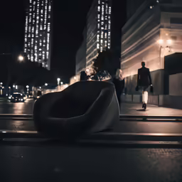 a black and white photo of a person standing next to a building with an odd shaped couch sitting on a curb
