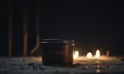 some candles sit in the dark beside a cup of coffee