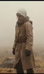 a man wearing a trench coat stands on top of a field