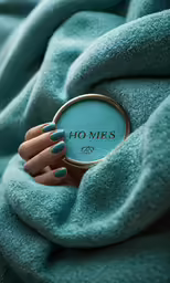 a woman holds out her manicures under a blue blanket