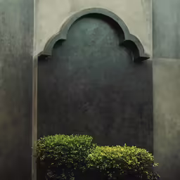 an archway with a stone pillar and trimmed plant