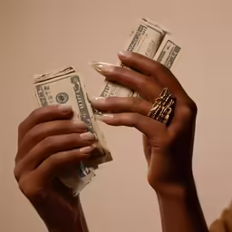 woman holding two stacks of cash and gold ring