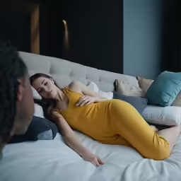 woman in yellow sitting on a bed with one arm outstretched