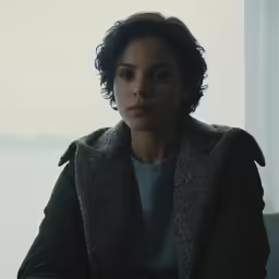a girl staring ahead, with her arms crossed, sits in front of an empty window