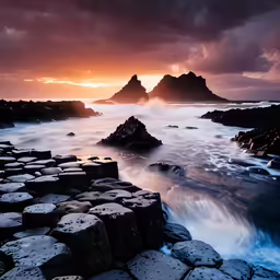 the sunset shining over the ocean with rocks in the foreground
