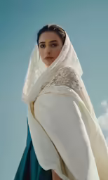 a woman standing against the blue sky, wearing a white veil
