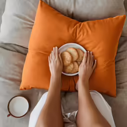 someone holding a bowl of cookies while sitting on the couch