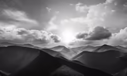 black and white photograph of mountains, clouds, and the sun