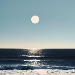 the sun shines bright on the ocean with a large disc over it