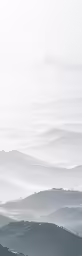 a group of hills covered in fog under a gray sky