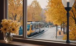 a window with a train passing by, and yellow trees outside