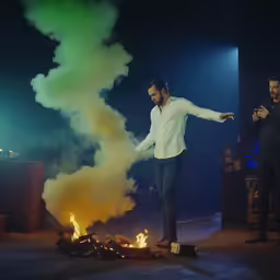 man in white shirt standing at open fire with two other men