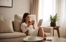 a woman in her twenties sitting on a couch playing with a cell phone