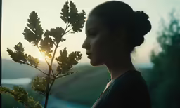 a young woman stands next to a tree as the sun shines