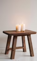 two lit candles sit on an old, rustic wood stand