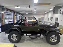 a green jeep parked in a garage next to another car,the jeep is black in color, and has a leather seat