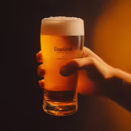 a person holding up a tall beer glass in front of a dark background