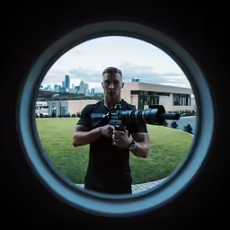 a man holds a large camera in a round window