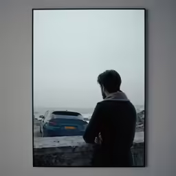 a man looks over an oceanwall from behind a car