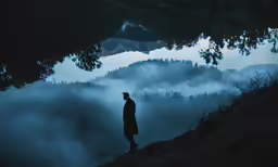 man on mountain looking at misty landscape and water