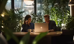 two people are working on their laptops in a large plant filled area
