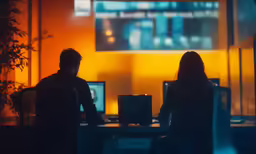 two people sitting at a desk working at computers