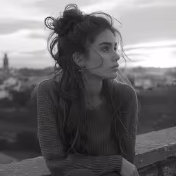 a black and white photo of a woman sitting on a wall,young woman sitting and gazing at sunset in black and white photo