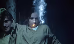 a young woman has her hand on the face of a man in robes, while a light emits out behind her
