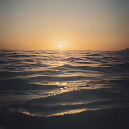 the sun shining through an orange sky over the ocean