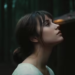 a young woman stares to the side in a dark forest