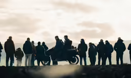 group of people gathered around a motorcycle near the ocean