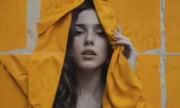 a beautiful young woman hides her face in a yellow cloth