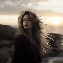 a woman standing on a hillside with her hair blowing,a woman in black dress with wind blowing her hair