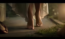 a barefoot woman walking on the grass next to her purse