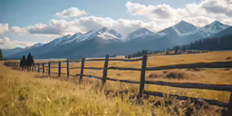 two people riding horses along the side of a wooden fence