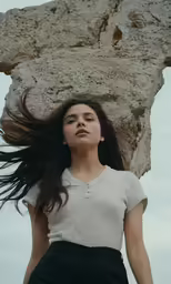 a woman is holding her hair next to the rock