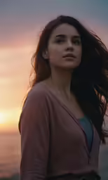 a woman is standing by the ocean at sunset
