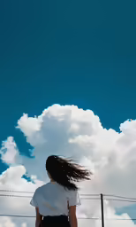 a woman walks under a cloudy blue sky