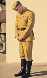 an uniformed soldier is looking down while standing in front of a yellow wall