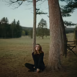 a woman sits under a tree in the grass