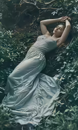 a woman laying in the woods in an elegant white dress