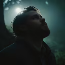 a man standing in the middle of a forest looking up at the sun