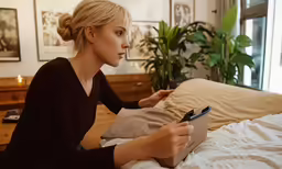 the woman sitting on her bed looks at a cell phone