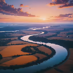 a river running through a green countryside under a sunset