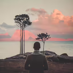there is a man standing by the water watching the sunset