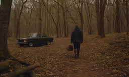 a man walking down a trail past parked cars