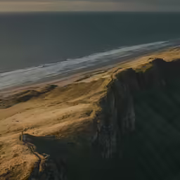 an aerial shot of an ocean cliff beach and the horizon